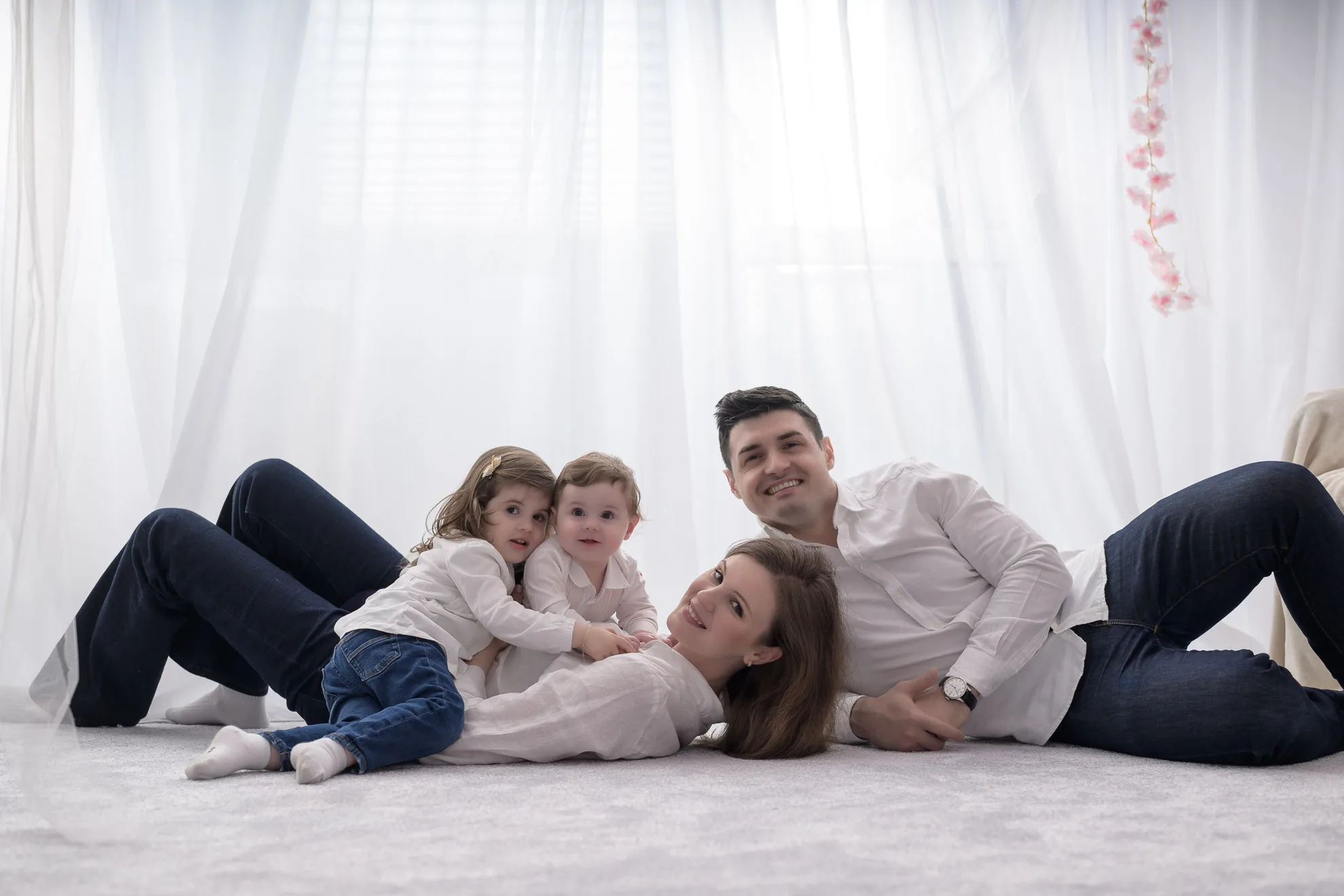 Parinti si copii imbratisati pe covor alb in lumina naturala, sedinta foto familie bucuresti calda si intima